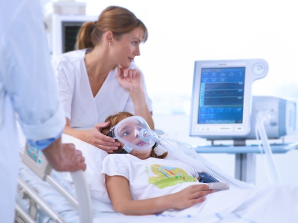 Das Philips Respironics V60 Beatmungsgerät wird mit einer Philips Respironics Performax Ganzgesichtsmaske auf Intensivstationen zur stationären Beatmung verwendet. Das Krankenhauspersonal hat einen guten Überblick am Bildschirm des Philips Respironics V60 Beatmungsgeräts.