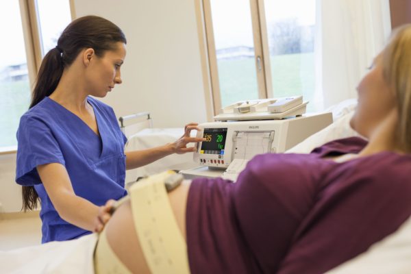 Eine Hebamme bedient einen Fetalmonitor. Die Philips Avalon CL Basisstation steht auf dem Monitor. Im Vordergrund ist der Bauch einer Schwangeren zu sehen.